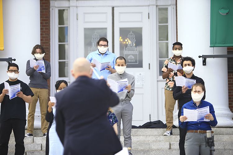 Wearing masks, a chorus sings on steps in front of Boyden Hall.