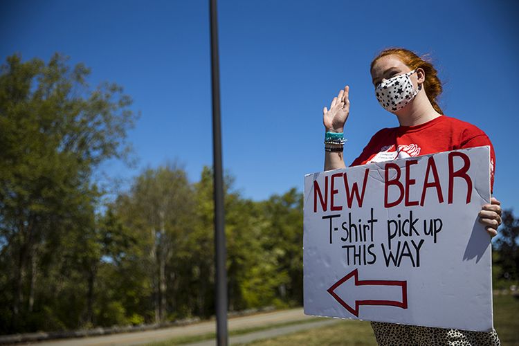 A student wearing a mask holds a sign directing people to “New Bear T-Shirt Pickup.”