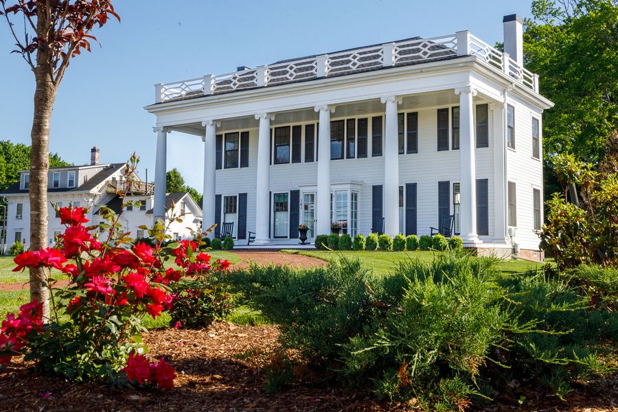    The exterior of the white Martin Richard Insitute for Social Justice house with a tree and flowers in the foreground.