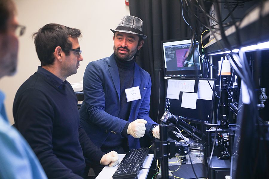A professor explains photonics equipment to two other people standing in a lab.