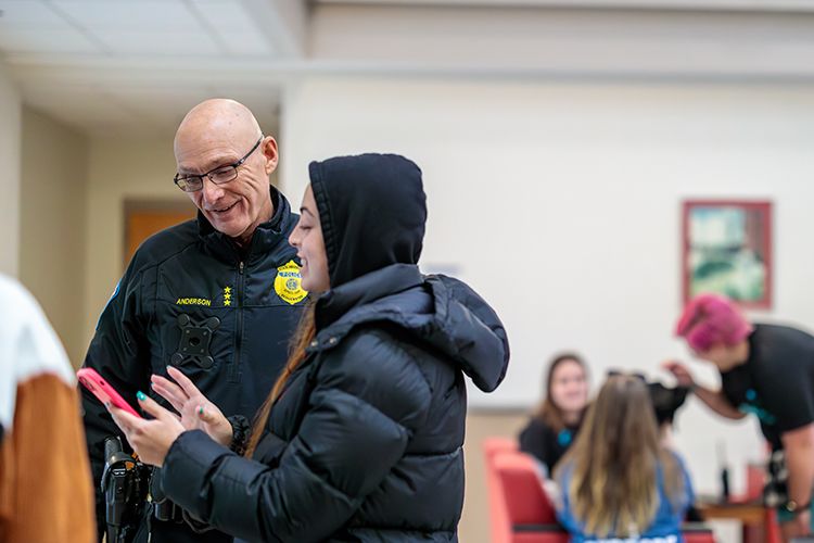 Standing in a lobby, a student and police officer look at a phone screen.