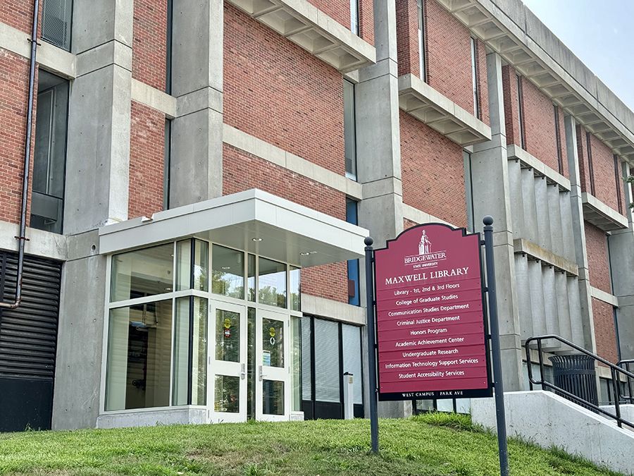 The exterior of Maxwell Library, including a red sign identifying departments in the building and a renovated glass entry.