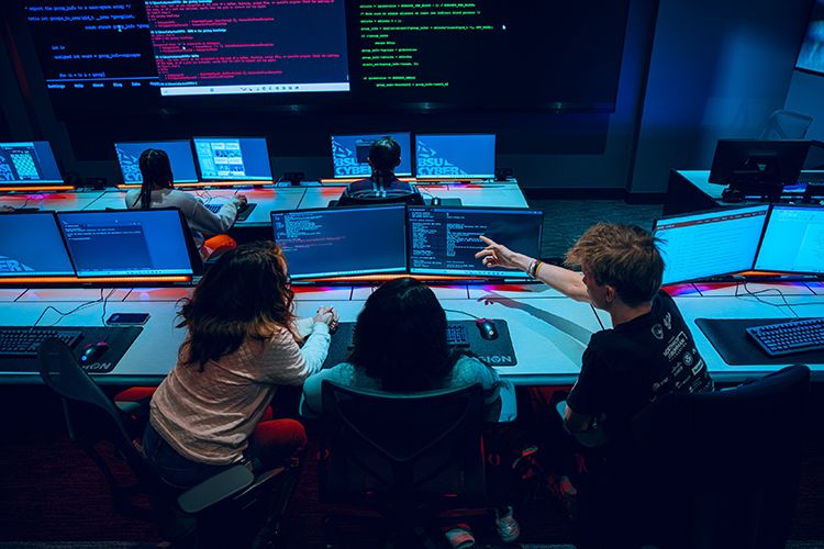 In the cyber range, three students work at computer monitors.