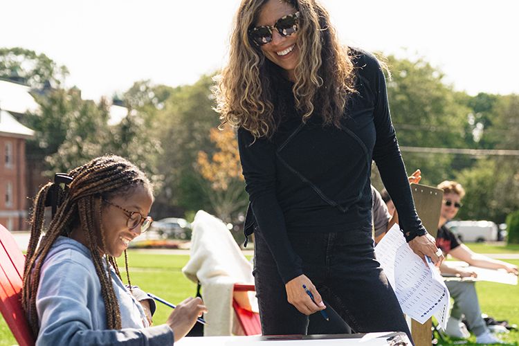 On the campus quad, a professor and student smile while looking at the student’s artwork.