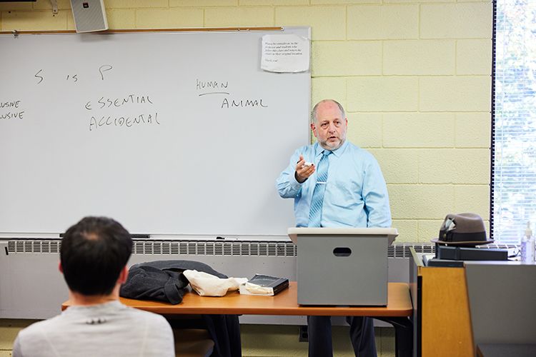 A professor lectures while standing in front of a white board.