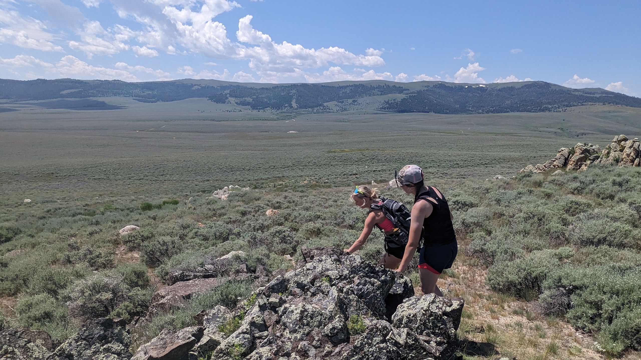 Two students walk next to rocks with a mountain range in the distant background.