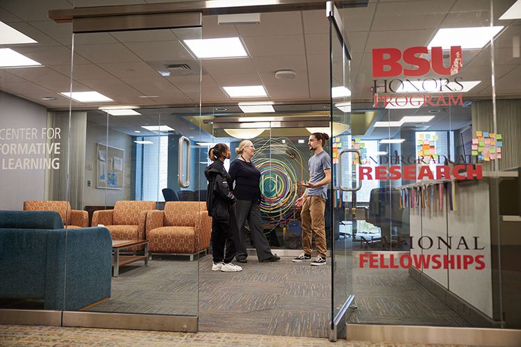 Three people talk while standing behind a glass wall with an open door to the Center for Transformative Learnig.