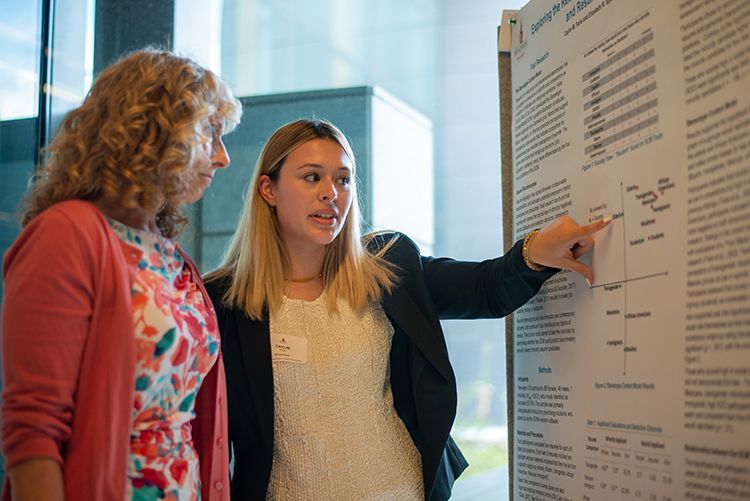 A student points to an item on an academic poster while a second person looks on.