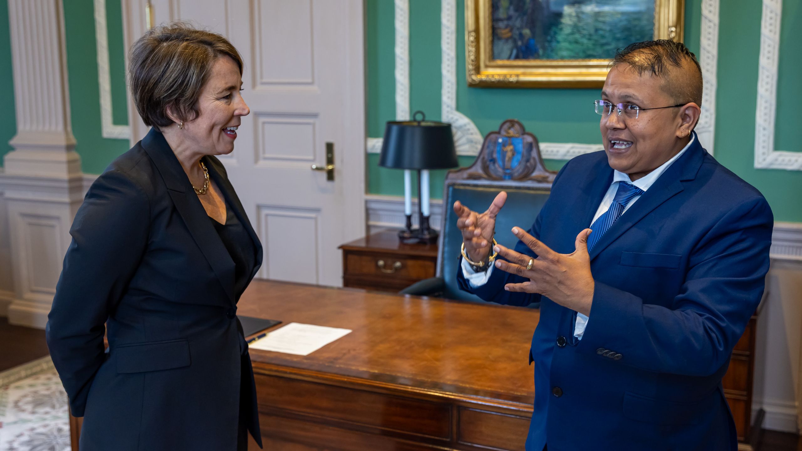Cindy Mack talks with the Massachusetts governor in front of a desk.