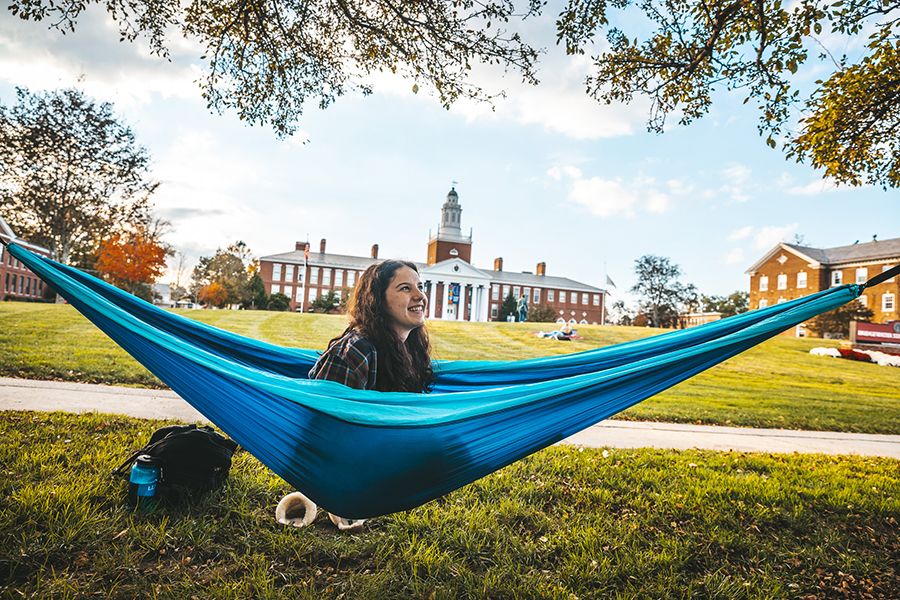 A student smiles while sitting in a hammock in front of Boyden Hall. 