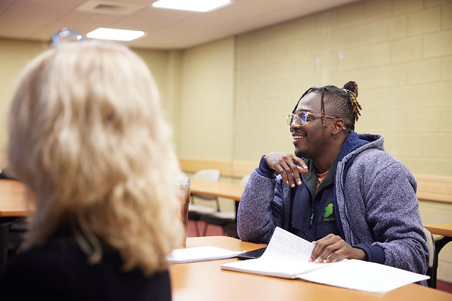 A student smiles while sitting at a classroom desk.