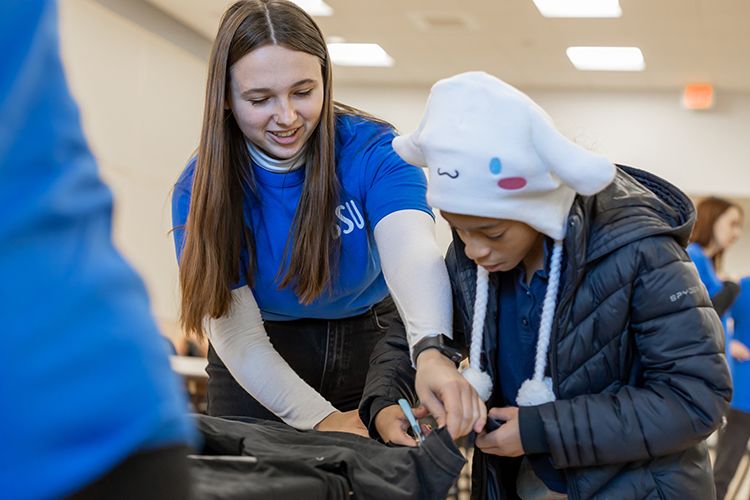 A BSU student helps a child cut a cloth using scissors.
