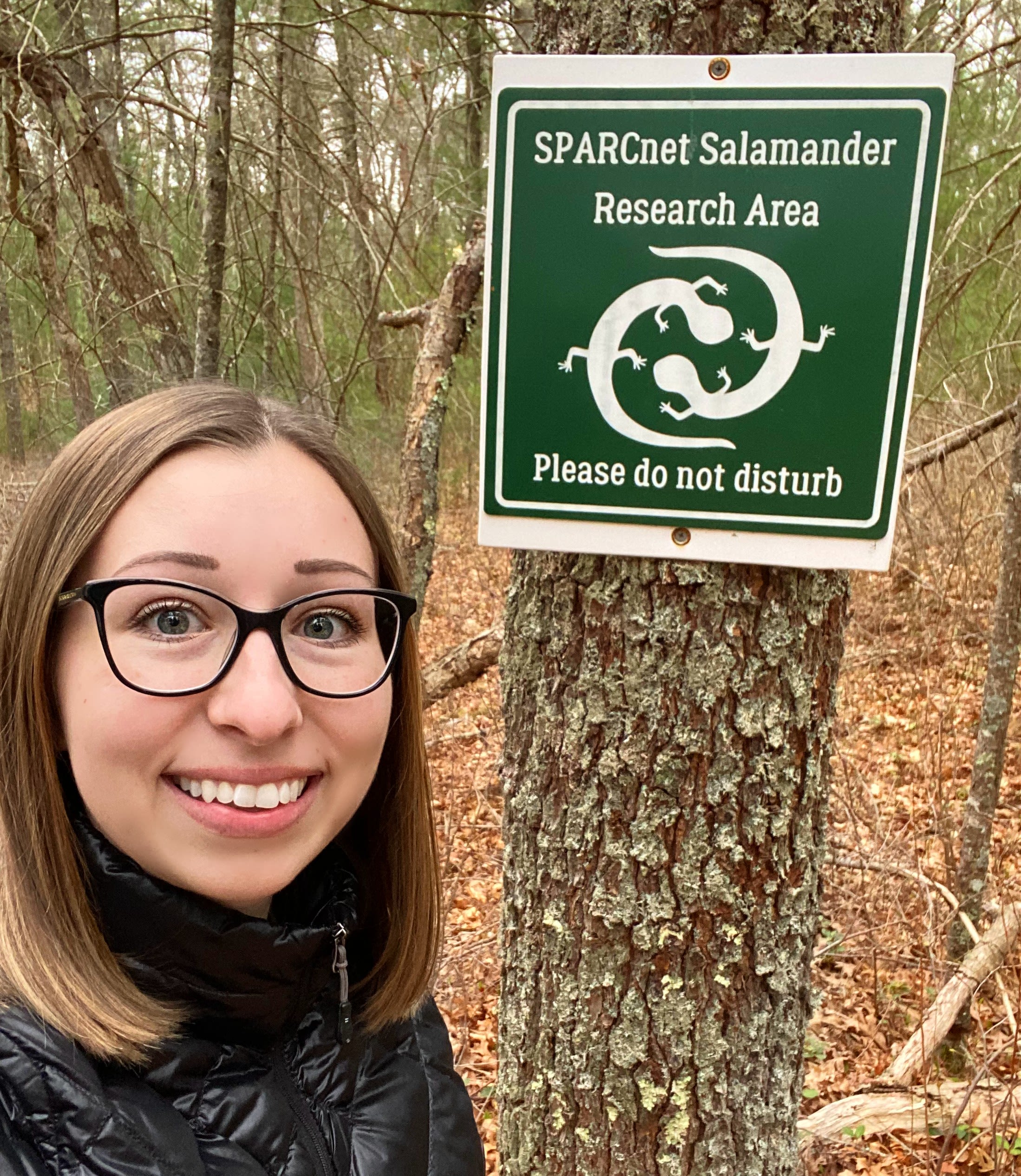 Julia Whalen standing in the woods next to a sign for a salamander research area.
