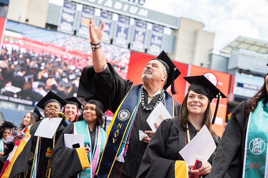 In a graduation procession of students, one gestures to the crowd.