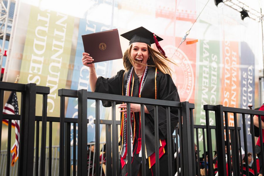An excited student holds up her diploma after crossing the commencement stage.