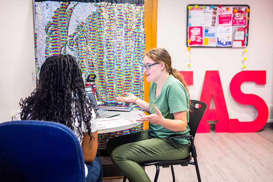 Two students talk while sitting at a table in Student Accessibility Services.