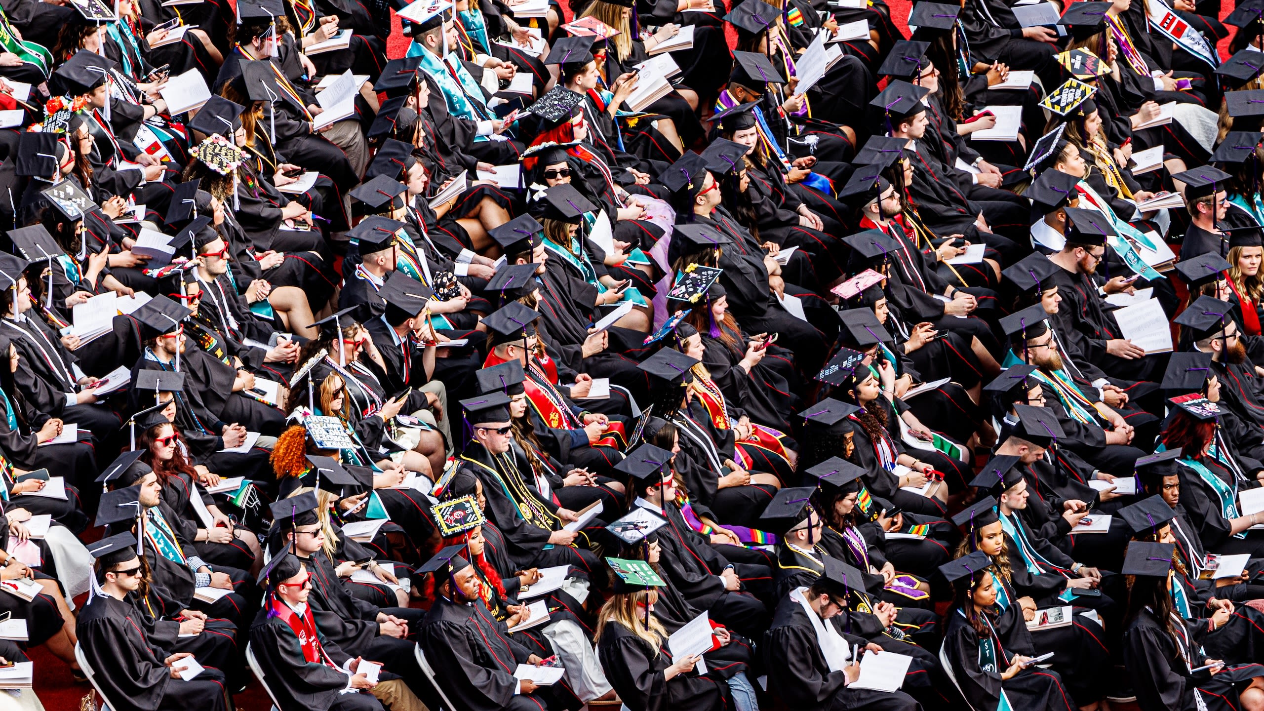 Aerial view of many graduates sitting in rows in their caps and gowns.