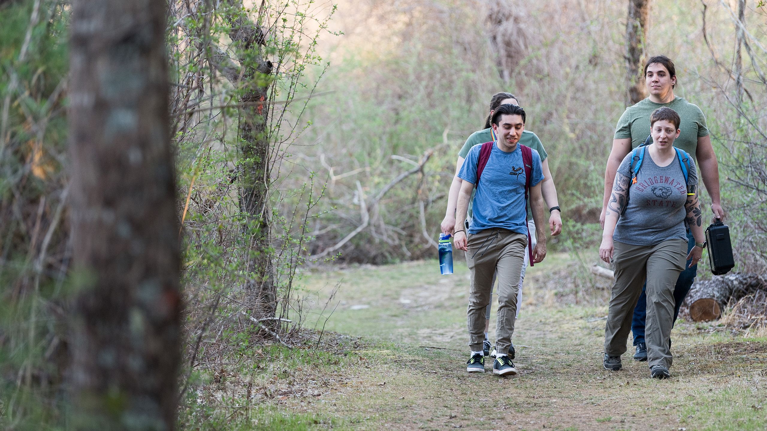 A professor and several students walk on a path in the woods.