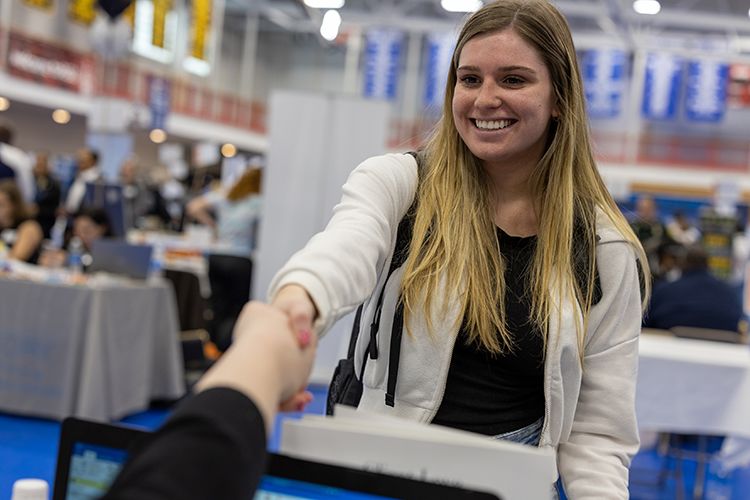A smiling student shakes a job recruiter's hand at a career fair.
